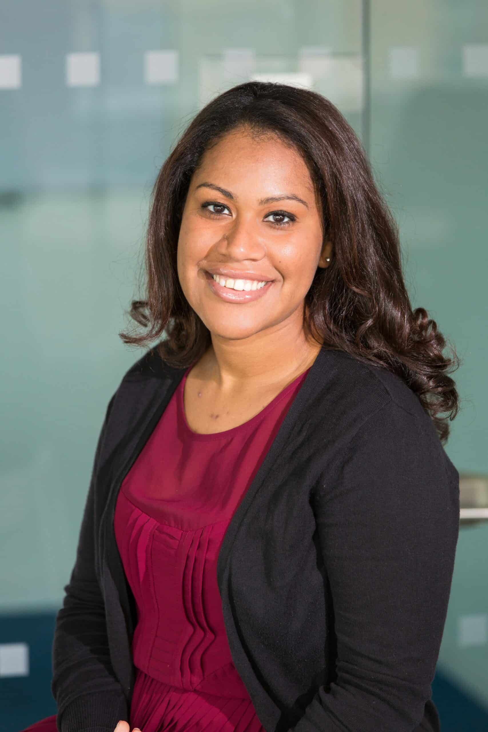 Confident woman smiling, wearing formal attire in a corporate environment.