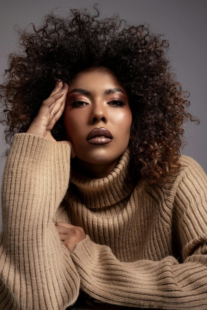 Close-up portrait of a woman in a cozy turtleneck sweater with a striking curly hairstyle.